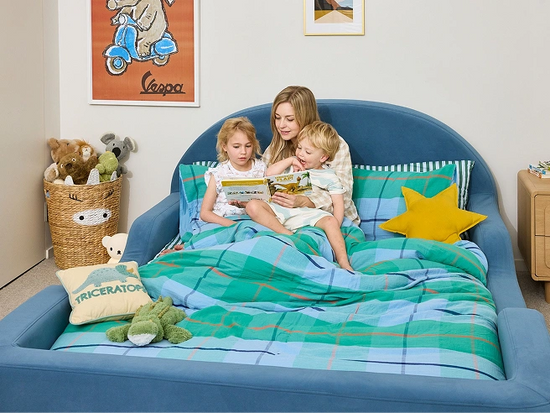 Woman and two children reading a book on a blue bed in a child-friendly room.